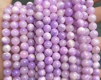 Puede incluir: Una hebra de cuentas redondas de piedras preciosas de color púrpura y blanco. Las cuentas tienen un acabado liso y pulido y están enhebradas en un hilo transparente.