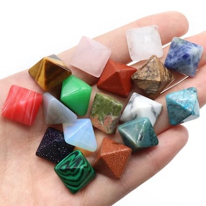 May include: A selection of small, pyramid-shaped gemstones with square bases, in a variety of colours and patterns. The gemstones include red, green, blue, brown, and white, some with unique textures and veining.