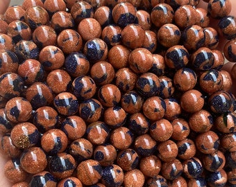 May include: A close-up of a pile of round, brown and blue gemstone beads. The beads are smooth and have a speckled appearance.