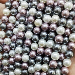 May include: A collection of round, pearl-like beads in shades of white, grey, and pink. The beads are smooth and glossy, and they are arranged in a random pattern.