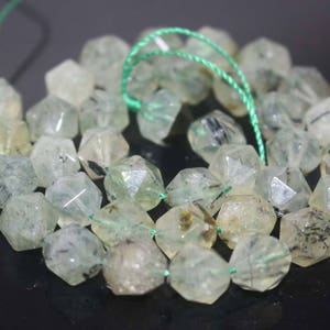 May include: A strand of green and black gemstone beads. The beads are faceted and have a translucent appearance. The beads are strung on a green thread.