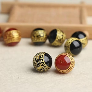 Puede incluir: Una colección de cuentas redondas con ribetes dorados y centros negros o rojos. Las cuentas tienen diseños intrincados y probablemente se utilizan para la fabricación de joyas.