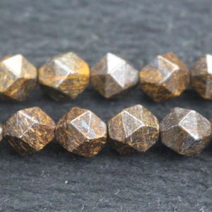 Könnte beinhalten: Eine Strähne aus braunen und goldenen facettierten Edelsteinperlen. Die Perlen sind pyramidenförmig mit vielen Seiten und haben einen metallischen Glanz.