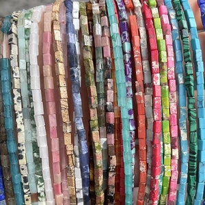 May include: Assortment of colorful square gemstone beads, strung on a thread. The beads are made of various natural stones, including turquoise, lapis lazuli, and malachite.