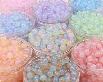 May include: Assortment of iridescent glass beads in various pastel colors, including pink, blue, green, and yellow, displayed in clear glass jars.