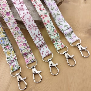 Peut inclure: Cinq porte-clés en tissu à motifs floraux avec des clips pivotants argentés. Les porte-clés sont dans des tons de rose, violet et vert.