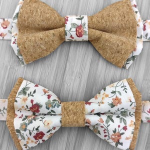 Peut inclure: Deux nœuds papillon avec un centre en liège et un tissu à motifs floraux. Les nœuds papillon ont un fond blanc avec des fleurs rouges, jaunes et vertes. Le bandeau du nœud papillon est également en liège. Le fond est en bois gris clair.