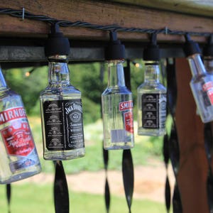 May include: A string of lights made from empty liquor bottles, including Smirnoff Vodka and Jack Daniel's Tennessee Whiskey, hanging from a wooden pergola.