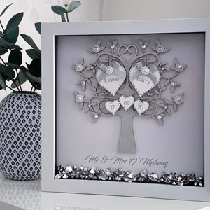 May include: A framed, grey, decorative tree with heart-shaped leaves and embellishments. The names "Elaine" and "Barry" are on heart-shaped leaves. The date "12 09 20" is also displayed. The frame is white, and the bottom has decorative crystals. The text "Mr & Mrs O'Mahony" is at the bottom.