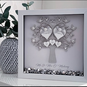 May include: A grey framed picture with a silver glitter tree and two hearts with the names Elaine and Barry. The tree has smaller hearts with the dates 12, 09, and 20. The bottom of the frame has silver glitter and the text "Mr & Mrs O'Mahony".