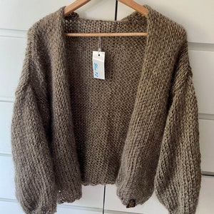 May include: A brown knitted cardigan with a loose fit and long sleeves. The cardigan is hanging on a wooden hanger with a "Blue72" tag.