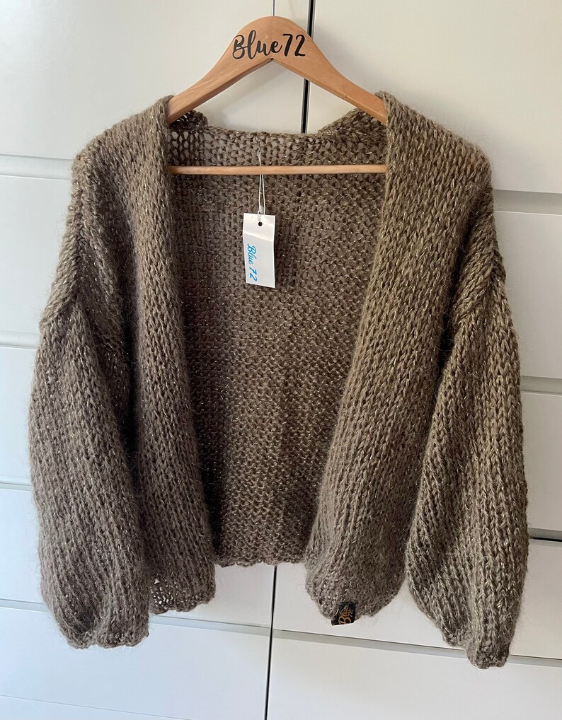May include: A brown knitted cardigan with a loose fit and long sleeves. The cardigan is hanging on a wooden hanger with a "Blue72" tag.