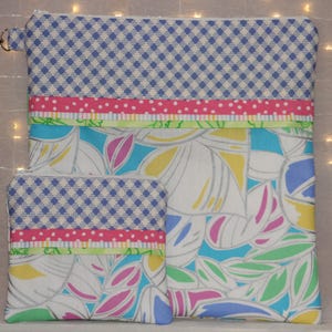 Puede incluir: Un conjunto de dos bolsas de tela. La bolsa m&aacute;s grande tiene una cremallera y un peque&ntilde;o cierre plateado. Ambas bolsas presentan un patr&oacute;n de cuadros azules y blancos, cinta rosa de lunares y un dise&ntilde;o floral con hojas blancas, azules, amarillas y rosas.