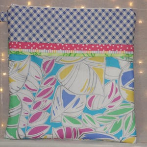 Puede incluir: Bolsa con cremallera colorida con una parte superior de cuadros azules y blancos, una franja rosa con lunares y un estampado floral en tonos azules, verdes, rosas y amarillos. La bolsa tiene un tirador de cremallera plateado.