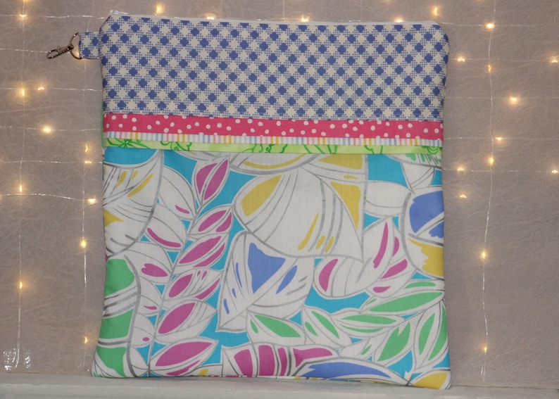 Puede incluir: Bolsa con cremallera colorida con una parte superior de cuadros azules y blancos, una franja rosa con lunares y un estampado floral en tonos azules, verdes, rosas y amarillos. La bolsa tiene un tirador de cremallera plateado.