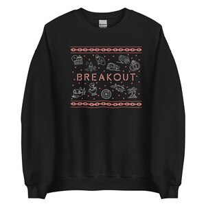 May include: Black sweatshirt with a white outline of a chain link pattern and various icons, including a building, a person, a train, and a palm tree. The text "BREAKOUT" is in pink.