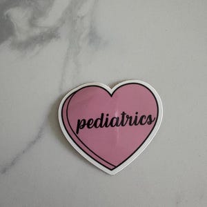 May include: A pink heart-shaped sticker with the word "pediatrics" in black script. The sticker has a white border and is set against a light gray background.