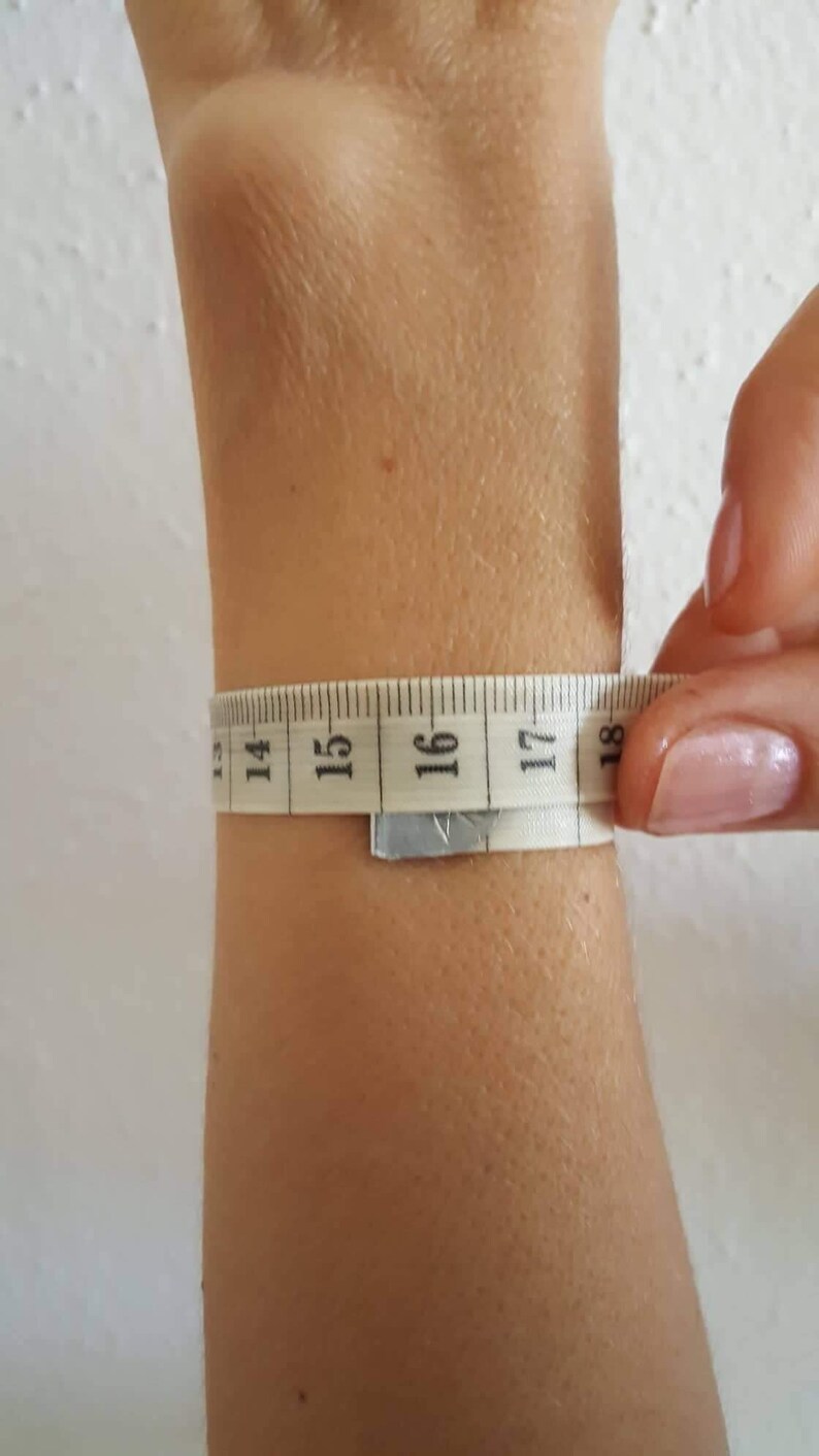 May include: A white measuring tape wrapped around a person's wrist, showing a measurement of 16 inches.