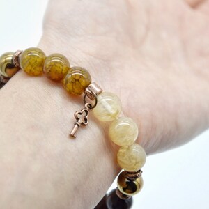May include: A bracelet with brown, yellow, and gold beads, a key charm, and a copper clasp.