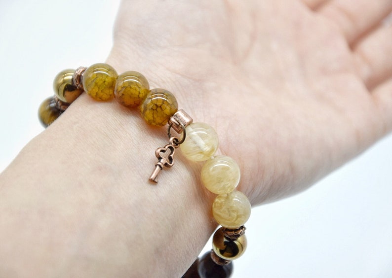 May include: A bracelet with brown, yellow, and gold beads, a key charm, and a copper clasp.