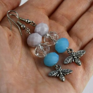 May include: A pair of dangle earrings with silver tone bee charms. The earrings feature light blue, clear, and lavender glass beads.