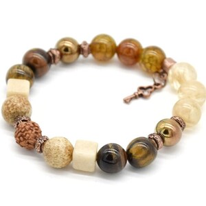 May include: A brown, beige, and gold beaded bracelet with a copper key charm. The bracelet features tiger's eye, wood, and other natural stones.
