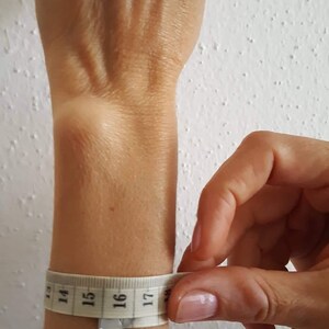 May include: A white measuring tape wrapped around a person's wrist, showing a measurement of 16 inches.