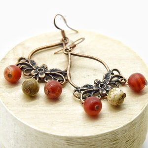 May include: Copper dangle earrings with a floral design and red, brown, and white agate beads.
