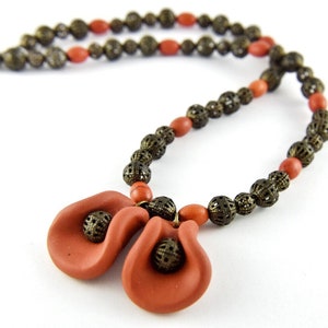 May include: A terracotta necklace with two large, sculpted terracotta pendant flowers. The necklace is made with small, round, bronze beads.