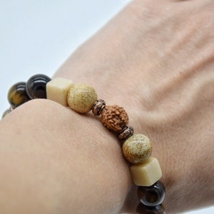 May include: A brown, black, and cream beaded bracelet with a copper accent. The bracelet is made with tiger's eye, wood, and rudraksha beads.