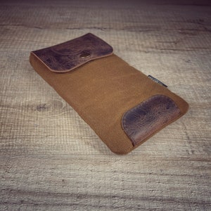May include: A brown canvas pouch with a leather flap and a brown leather patch on the bottom. The pouch has a brass button closure.