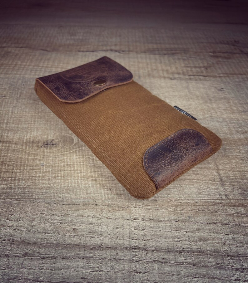 May include: A brown canvas pouch with a leather flap and a brown leather patch on the bottom. The pouch has a brass button closure.