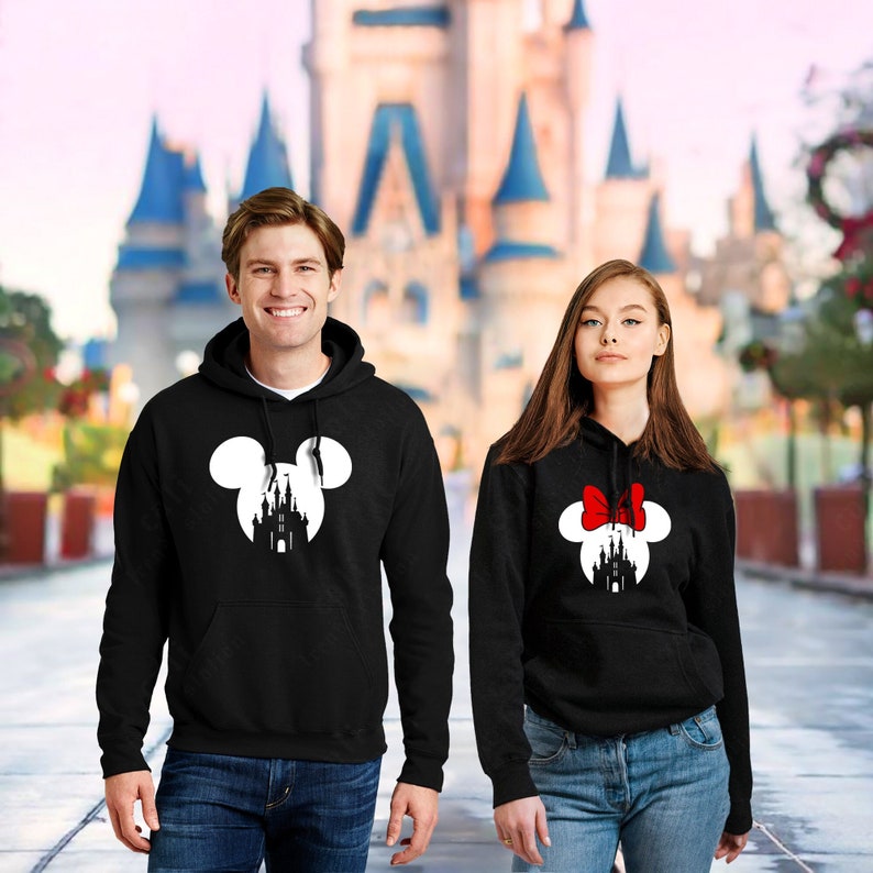 May include: A black hoodie with a white silhouette of Mickey Mouse ears with a castle inside the ears. A black hoodie with a white silhouette of Minnie Mouse ears with a castle inside the ears and a red bow on top.