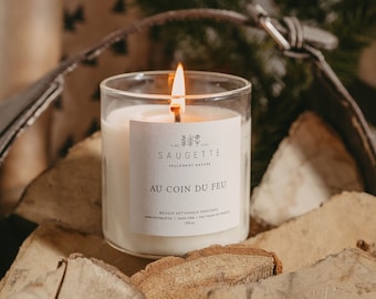 May include: A white candle in a glass jar with a label that reads "Saugette Seulement Nature Au Coin Du Feu"  Bougie Artisanale Parfumée Sans Phtalates 200g. The candle is sitting on a pile of wood logs.