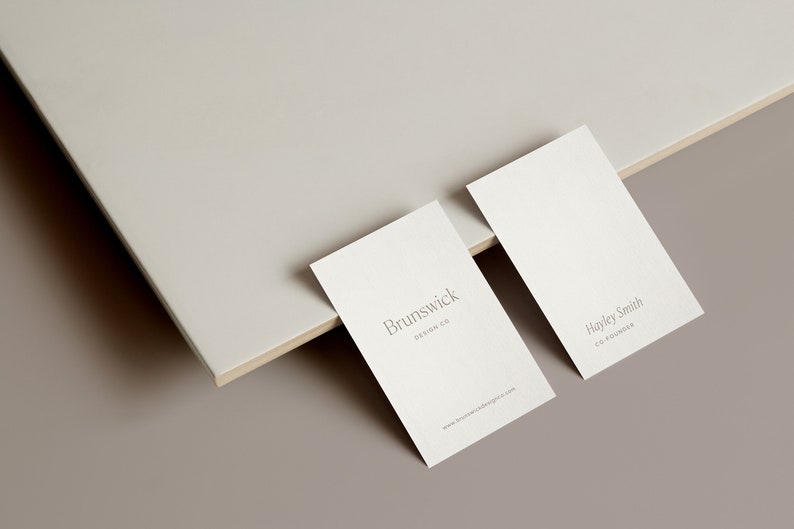 May include: Two white business cards on a light brown surface. The top card has the text "Brunswick Design Co." The bottom card has the text "Hayley Smith Co-Founder".