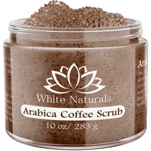 Puede incluir: Un tarro de vidrio de exfoliante de café Arábica marrón con un logotipo de flor de loto blanco y el texto "White Naturals Arabica Coffee Scrub 10 oz/ 283 g".