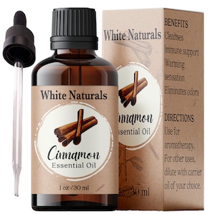 Könnte beinhalten: Eine braune Glasflasche mit einer Tropfpipette, gefüllt mit Zimt-Ätherischem Öl. Das Flaschenetikett lautet "White Naturals Cinnamon Essential Oil 1 oz / 30 ml". Das Etikett zeigt auch eine Zeichnung von Zimtstangen. Die Flasche steht neben einem braunen Karton mit dem Text "White Naturals Cinnamon Essential Oil" und einer Liste der Vorteile und Anwendungshinweise.