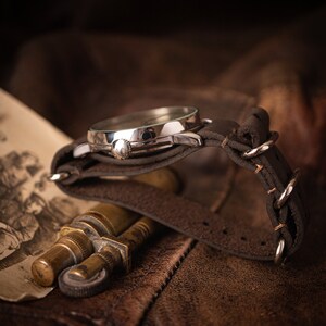 Puede incluir: Un reloj de pulsera plateado con una correa de cuero marr&oacute;n. El reloj est&aacute; sobre una superficie de cuero marr&oacute;n.