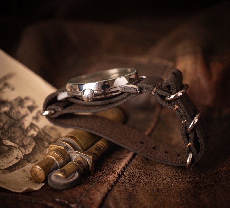 Puede incluir: Un reloj de pulsera plateado con una correa de cuero marr&oacute;n. El reloj est&aacute; sobre una superficie de cuero marr&oacute;n.