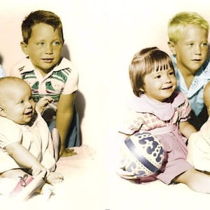 May include: A group of four children, two boys and two girls, are sitting together. The children are wearing colorful clothing and are smiling. The girl on the left is holding a blue and white ball. The boy on the right is wearing a green and white shirt.
