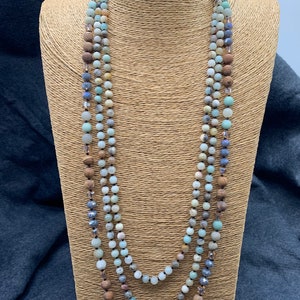 May include: A multi-strand necklace with light blue, brown, and gray beads. The necklace is made of various materials, including wood, crystal, and stone.