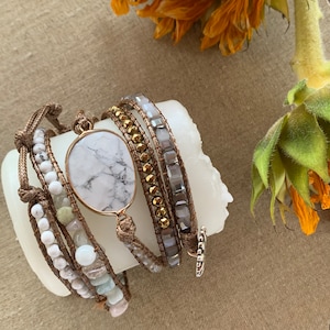 May include: A set of five bracelets with a white marble stone charm. The bracelets are made of brown leather cord, white beads, and gold and silver beads.
