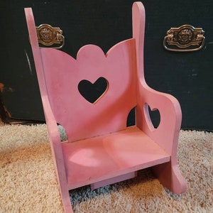 May include: A pink wooden rocking chair with a heart-shaped cutout in the back and two smaller heart-shaped cutouts on the sides.