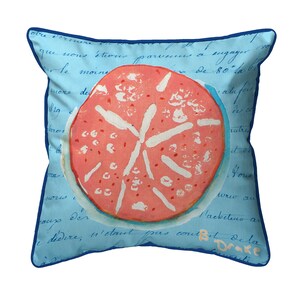 May include: A blue pillow with a white and pink sand dollar design. The pillow has a blue border and a handwritten message in black ink.