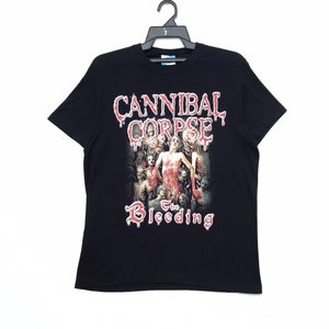 Op de afbeelding: Zwart T-shirt met een grafische print van de band Cannibal Corpse. De afbeelding toont een bloederige afbeelding van een bandlid en de woorden "The Bleeding".