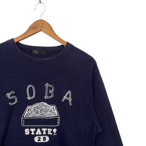 May include: A navy blue sweatshirt with a white graphic of a box of noodles and the text "SOBA STATE 28".