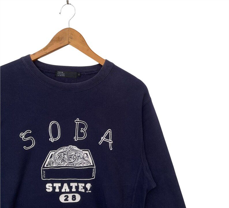 May include: A navy blue sweatshirt with a white graphic of a box of noodles and the text "SOBA STATE 28".
