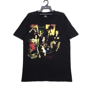 May include: Black t-shirt with a band graphic featuring a group of people sitting on a couch. The band's name "Aerosmith" is printed on the bottom of the graphic.