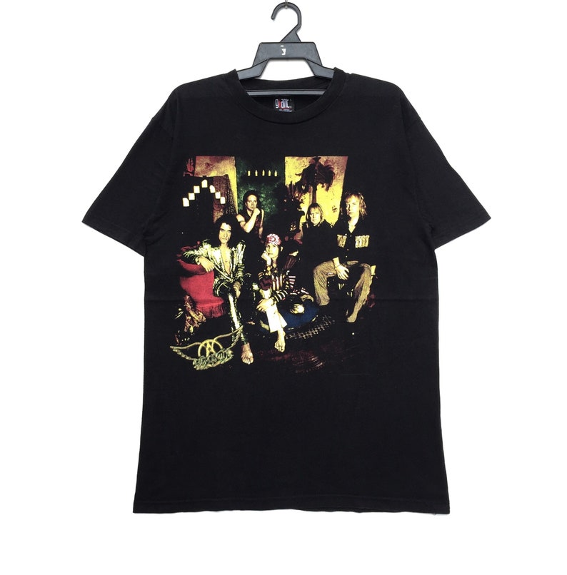 May include: Black t-shirt with a band graphic featuring a group of people sitting on a couch. The band's name "Aerosmith" is printed on the bottom of the graphic.