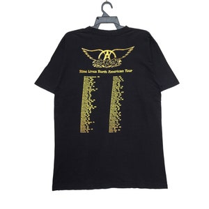 May include: Black t-shirt with a gold Aerosmith logo and the text "Nine Lives North American Tour" with a list of tour dates.